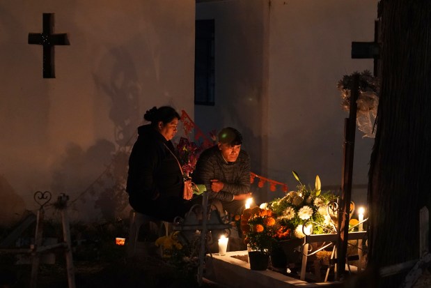 People sit by a tomb in the San Gregorio Atlapulco cemetery during Day of the Dead festivities on the outskirts of Mexico City, Wednesday, Nov. 1, 2023. In a tradition that coincides with All Saints Day on Nov. 1 and All Souls Day on Nov. 2, families decorate graves with flowers and candles and spend the night in the cemetery, eating and drinking as they keep company with their dearly departed. (AP Photo/Marco Ugarte)