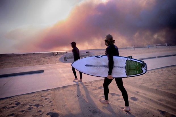 Surfers Shaun Rosenberg, right, and Teal Greene take to the waves under a blackened sky from a wildfire in the Pacific Palisades, during the sunset in Santa Monica, Calif., Tuesday, Jan. 7, 2025. (AP Photo/Richard Vogel)