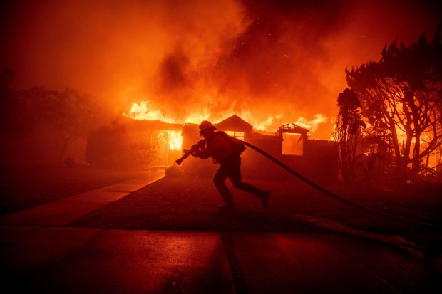 A firefighter battles the Palisades Fire as it burns a structure