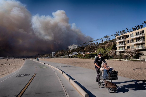 Jerome Krausse pushes his mother-in-law in a shopping cart as they evacuate from their home in the Pacific Palisades