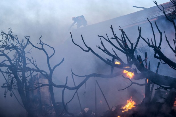 A firefighter tries to contain the Palisades Fire from a rooftop