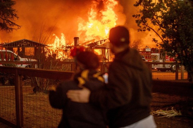 People watch as the Eaton Fire engulfs a structure Wednesday, Jan. 8, 2025, in Altadena, Calif. (AP Photo/Ethan Swope)