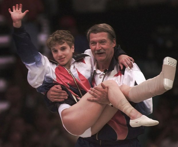 USA's Kerri Strug is carried by her coach, Bela Karolyi, as she waves to the crowd on her way to receiving her gold medal at 1996 Summer Olympics.